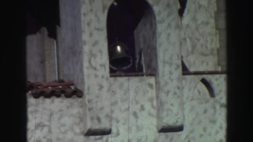 1969 Lake Tahoe-area home-movie frame of a white arched building facade, hanging bell, red tile trim, and visible film wear.