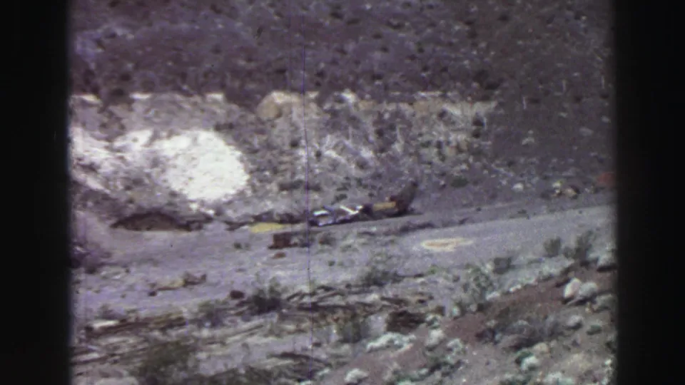 1969 Lake Tahoe home-movie frame showing rough hillside terrain, a pale ground patch, sparse vegetation, and a dirt path.