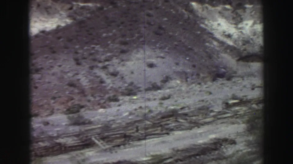 1969 Lake Tahoe frame showing a rocky slope, pale hillside area, rough dirt track, and scattered vegetation.