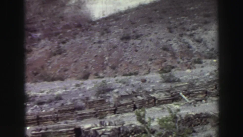 Lake Tahoe 1969 home-movie frame showing rugged hillside ground, sparse brush, a dirt track, and scattered wood or debris.