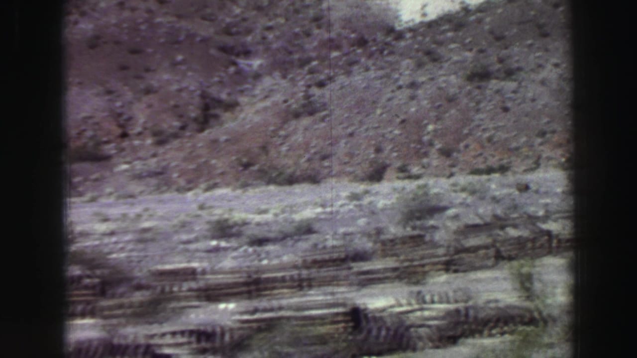 Rocky hillside with sparse brush and a wooden fence across the lower frame.