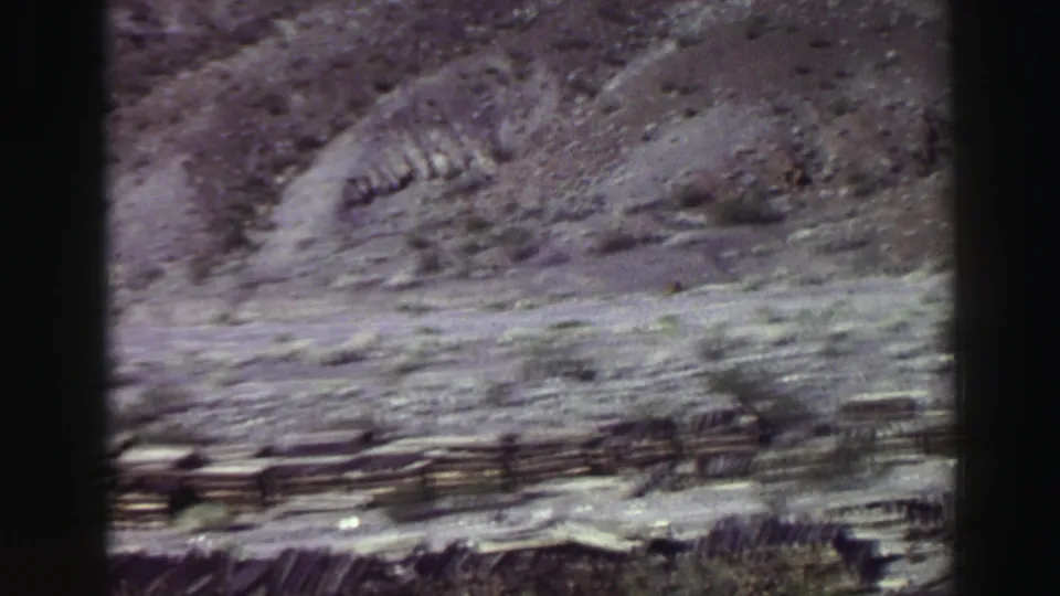 A motion-softened 1969 Lake Tahoe landscape frame shows a rocky bank, sparse brush, and a fence line near the lower foreground.
