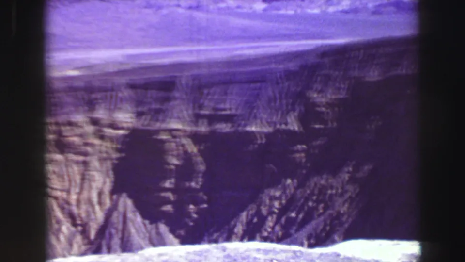 1969 8mm Lake Tahoe view with dark rock forms, rough cliff textures, and strong purple film coloration.