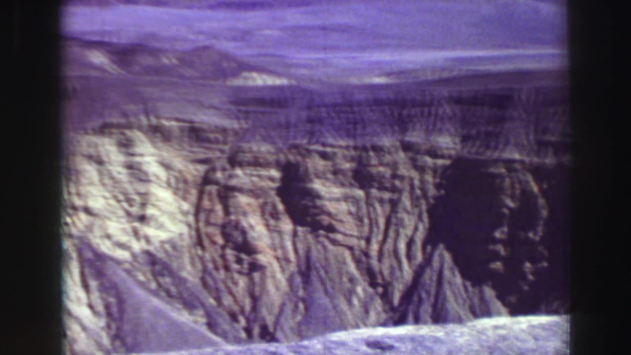 Layered canyon cliffs and pale rocky slopes seen through a dark 8mm film frame.