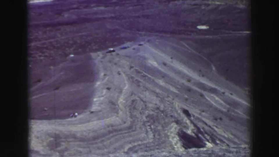 1969 8mm frame showing a dirt road across arid slopes with small distant vehicles in the Lake Tahoe travel-footage context.