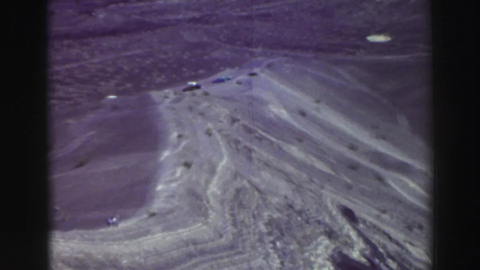 Color-shifted 8mm frame of arid canyon slopes, a winding road, and tiny vehicles, supported by Lake Tahoe, California metadata.