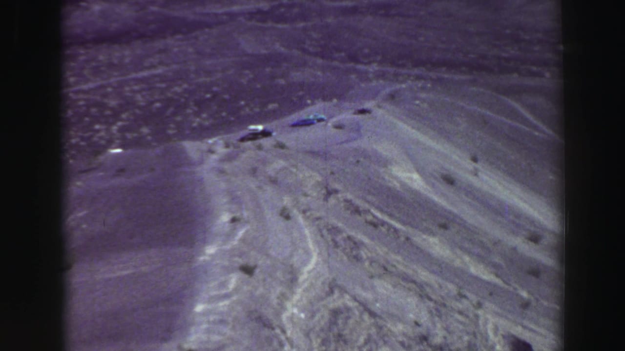Distant parked cars on a dusty ridge above a canyon landscape.