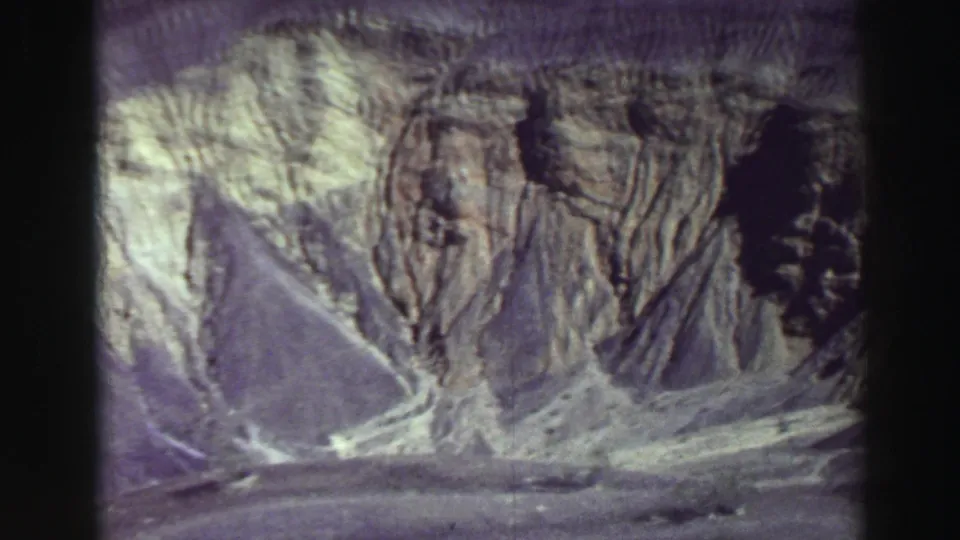 1969 8mm Lake Tahoe-area landscape frame showing steep ridged rock faces, pale slopes, and shadowed cuts in the canyon terrain.