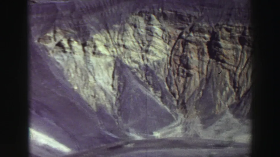 1969 8mm Lake Tahoe-area frame with a broad scree slope rising below layered cliffs and shadowed rock formations.