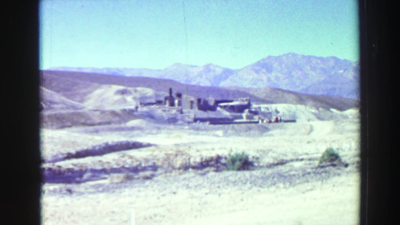 Wide view of dry hills with distant mountains and small ruins in the center.