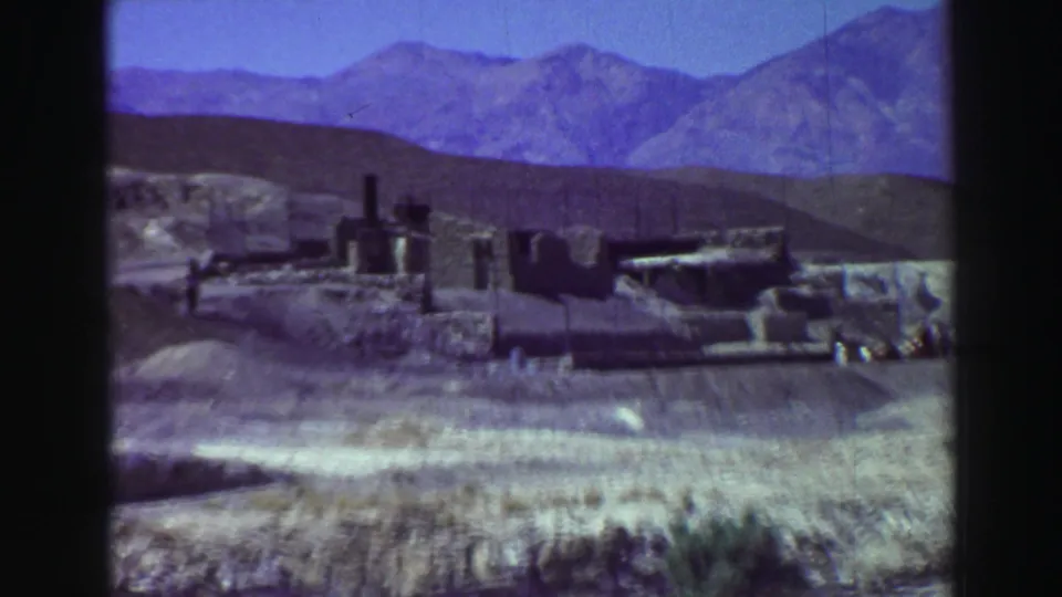 Closer 1969 home-movie view of weathered low walls and vertical ruin elements set against arid hills and mountains.