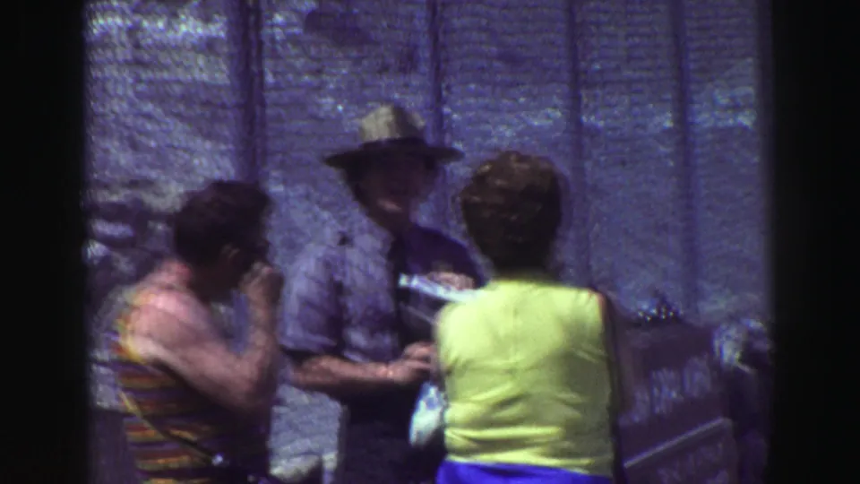 At the reported Lake Tahoe-area checkpoint, adults stand close to a chain-link fence while a uniformed man handles papers in soft 8mm color.