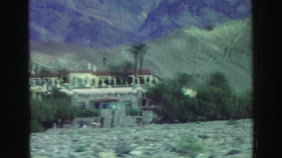 The final frame shows a low arched building with palms and scrub in front of rugged mountains, filmed from a distance on 8mm.