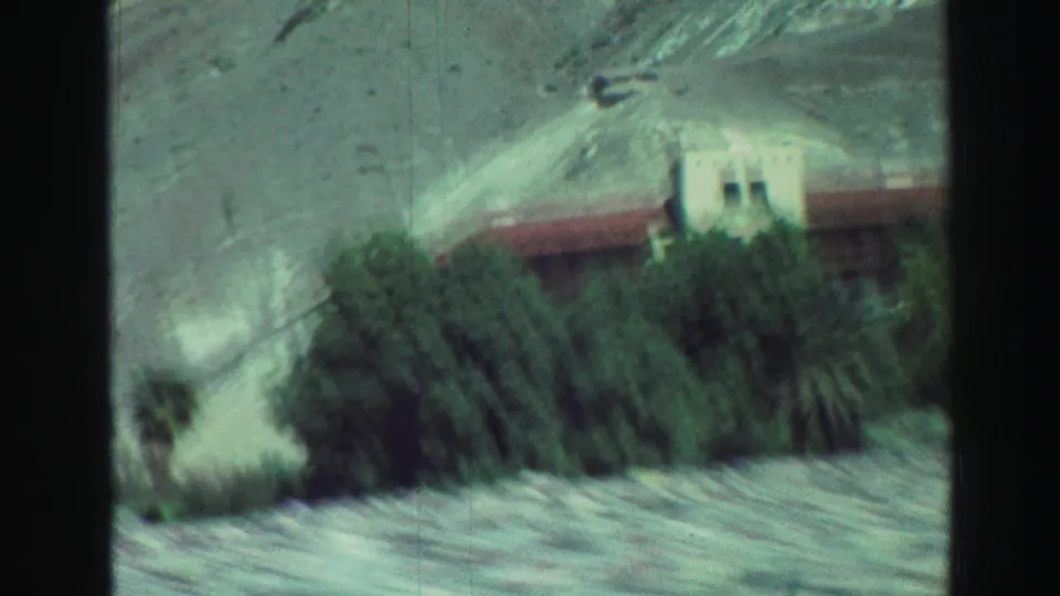1969 Lake Tahoe frame with a white structure and long red roof partly obscured by greenery below dry rocky mountain terrain.