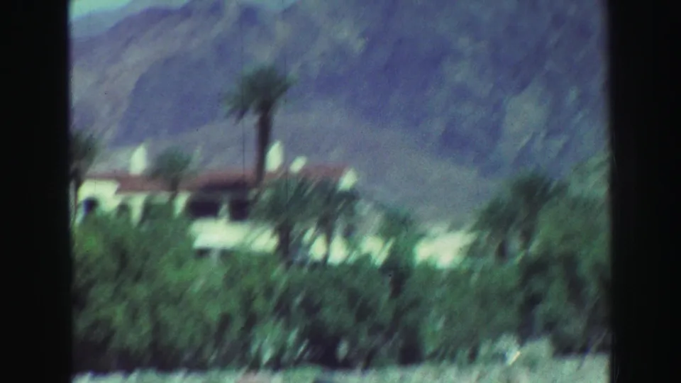 Blurred 1969 Lake Tahoe-area home-movie frame with a resort-like building partly obscured by palms and vegetation.