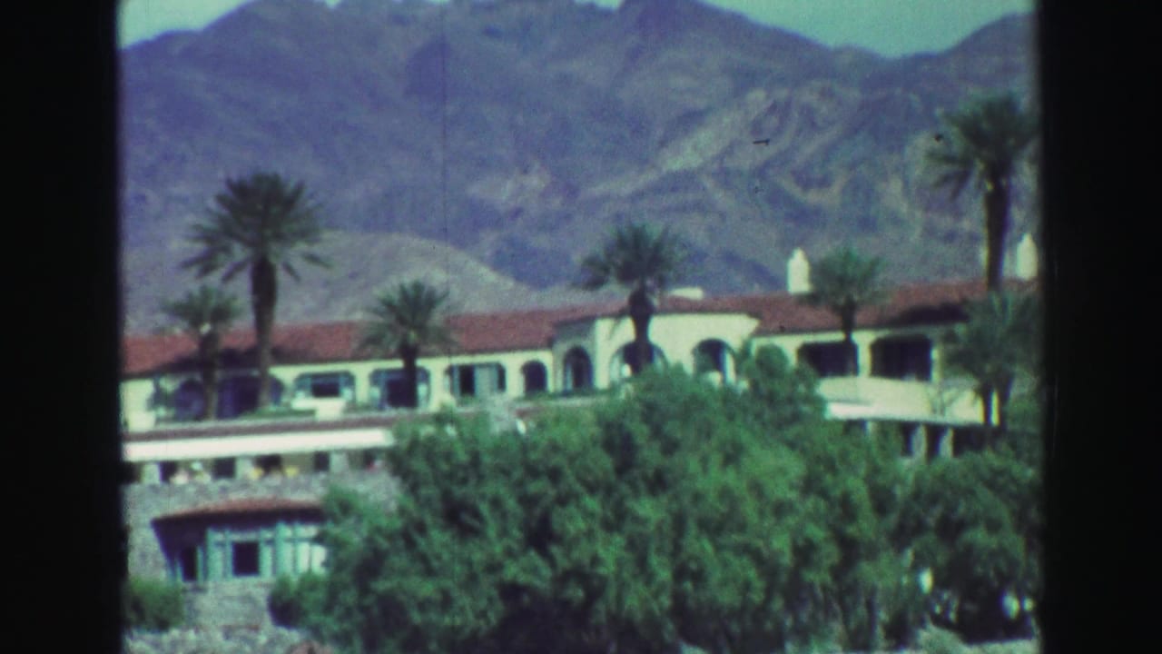 Spanish-style building with palm trees below desert mountains.