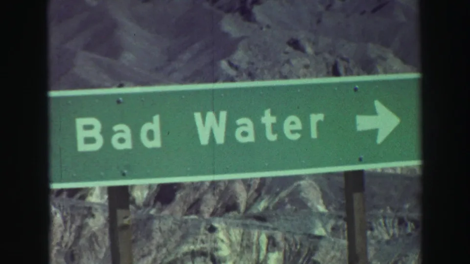 Close 8mm view of the Bad Water directional sign, with pale lettering and a right arrow against desert terrain.