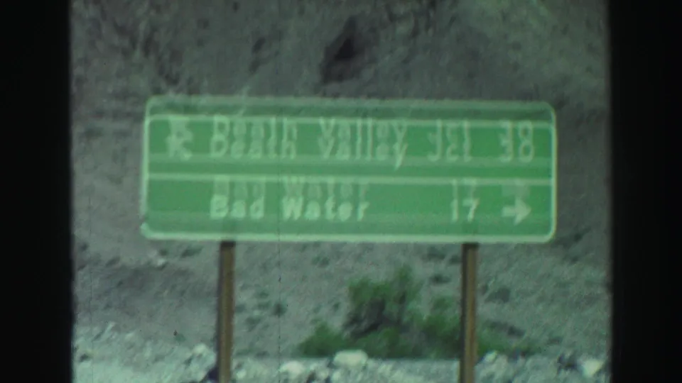 Green mileage sign lists Death Valley Junction and Bad Water directions in a desert roadside setting, exact location should be verified.