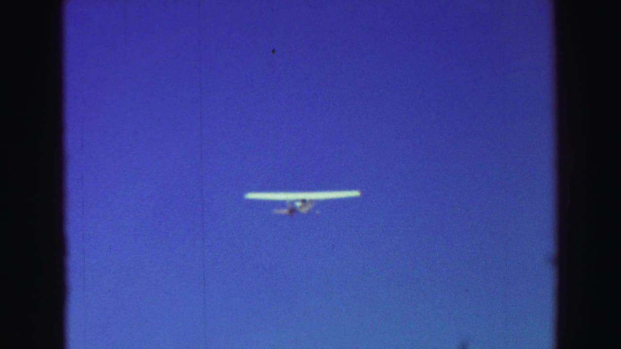 Small light aircraft flying against a deep blue sky with dark film borders.