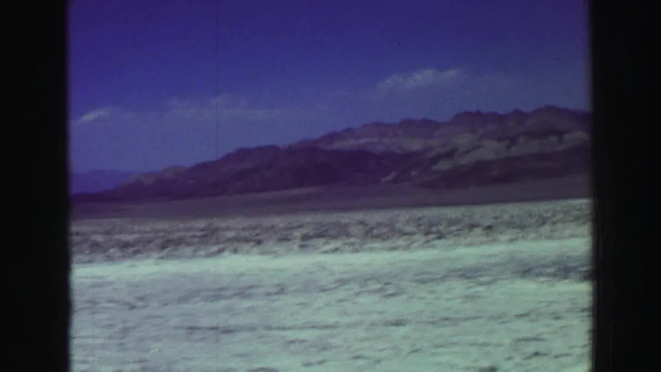 1969 Lake Tahoe 8mm frame with textured beach foreground, low scrub, distant mountains, and visible film gate edges.