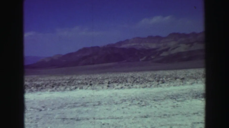 1969 Lake Tahoe 8mm frame showing a moving view over pale beach, scrub, and distant mountain slopes.