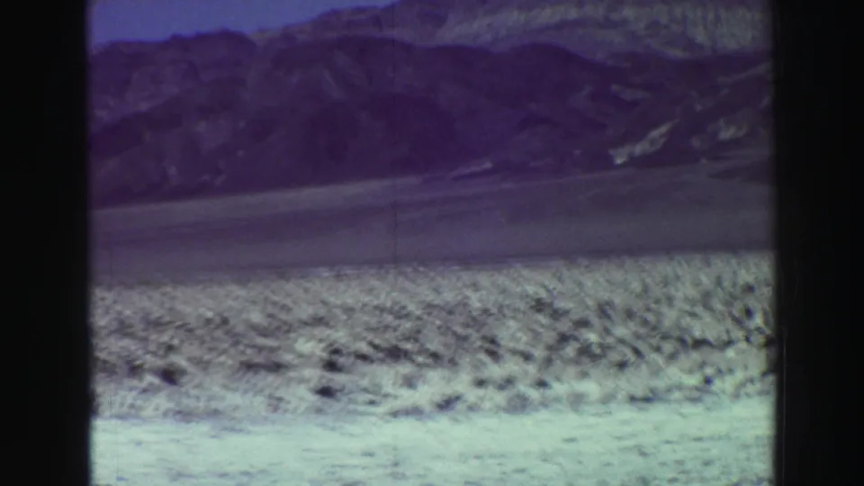 1969 Lake Tahoe 8mm frame with a closer mountain slope beyond a scrubby light shoreline and faded color cast.
