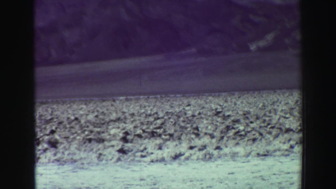 Distant mountains and rocky roadside seen through dark film gate borders.