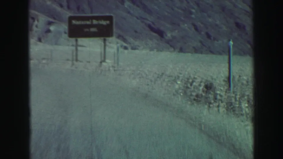 Roadside Natural Bridge sign along a curving mountain road in 1969 Lake Tahoe-area 8mm footage.