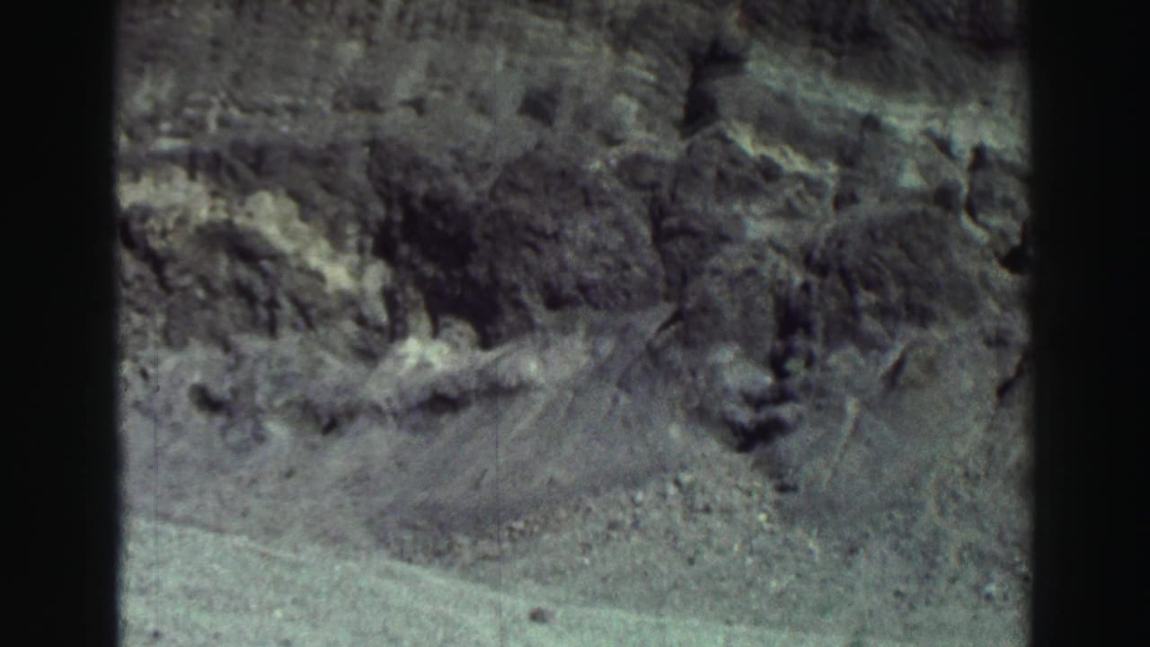 1969 8mm Lake Tahoe frame showing rugged rocks and pale shoreline ground with dark vertical film edges.