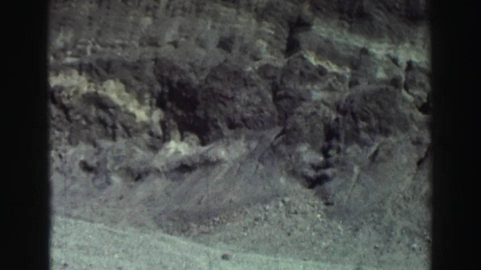 1969 8mm Lake Tahoe frame showing rugged rocks and pale shoreline ground with dark vertical film edges.