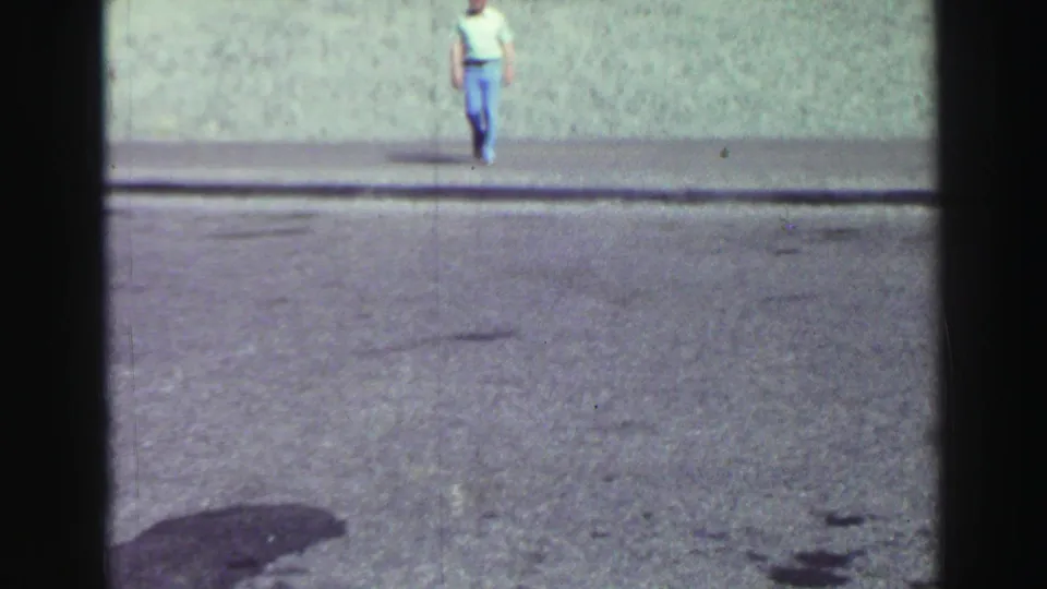 Distant adult man walking along a gravelly Lake Tahoe path beside a rocky outcrop in 1969 8mm footage.