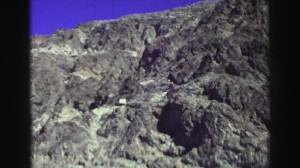 Lake Tahoe-area mountain terrain appears in faded 8mm color, with craggy rock, blue sky, and dark recesses.