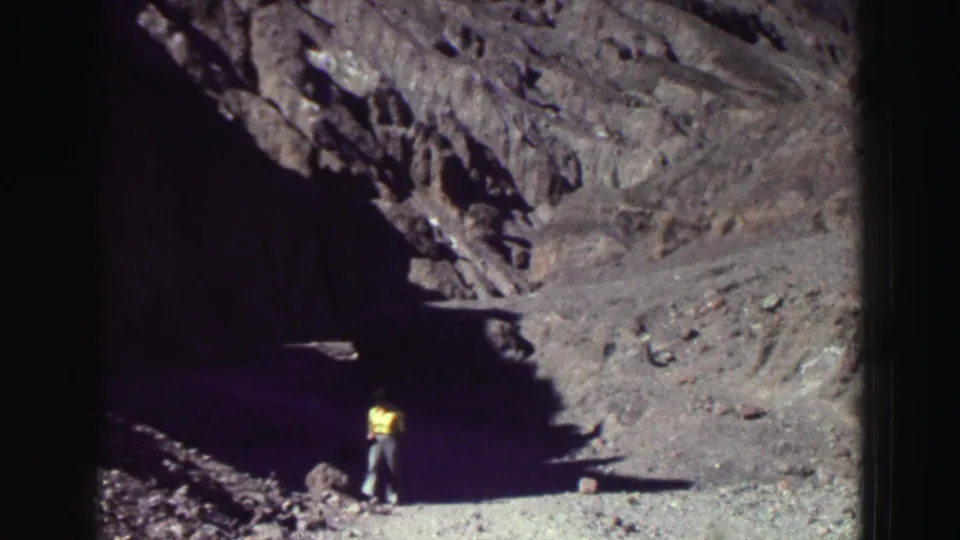 A lone person in a yellow shirt explores uneven ground near a dark rock opening in 1969 Lake Tahoe-area footage.