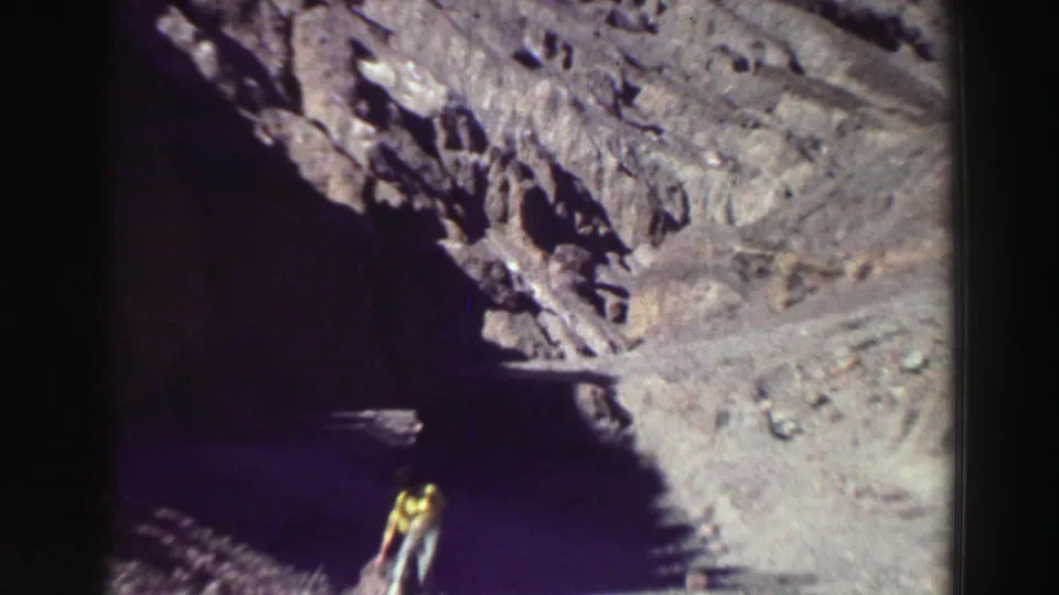 The 8mm frame shows a person moving near a shaded rock opening, dwarfed by the Lake Tahoe-area cliff formations.