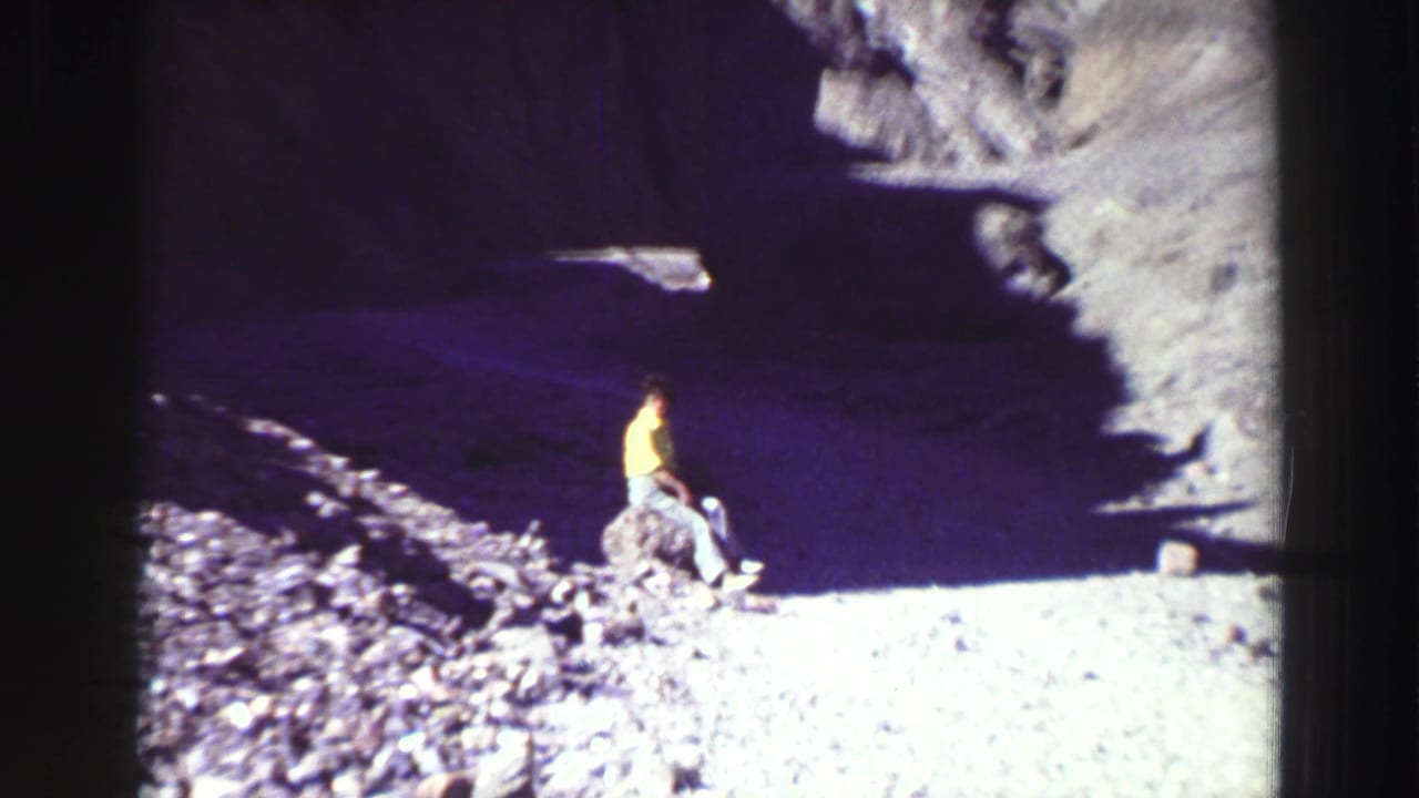 Person in a yellow shirt near a dark rocky cave entrance.