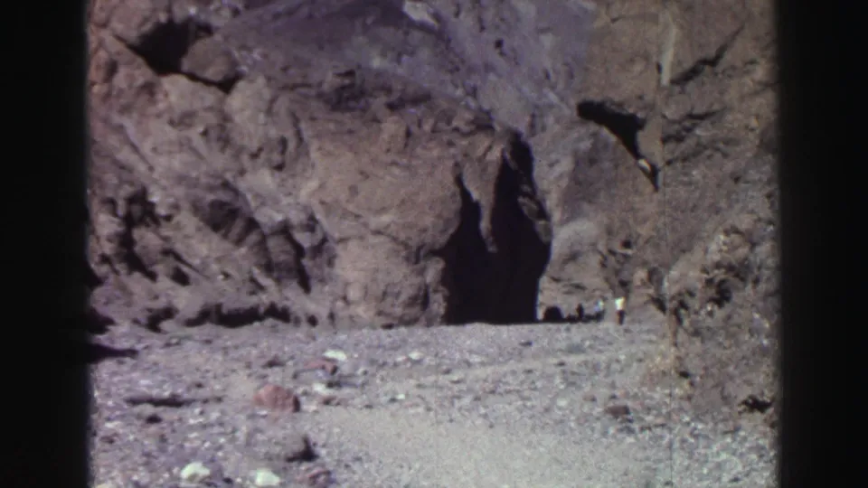 Lake Tahoe-area home-movie frame from 1969 showing rough stone, a cave-like shadowed entrance, and distant people beside the opening.