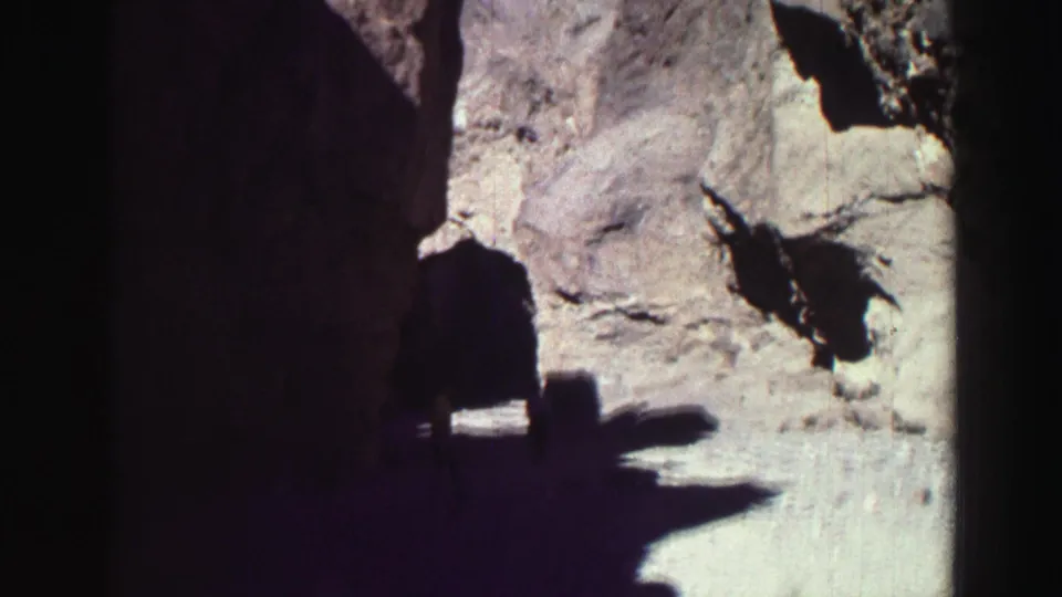 Handheld 1969 8mm view near Lake Tahoe approaching a shadowed rock opening, with bright stone and gravel visible ahead.