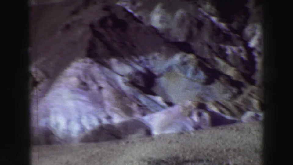 1969 Lake Tahoe home-movie frame with blurred rocky terrain, pale slopes, and strong purple-blue film color.