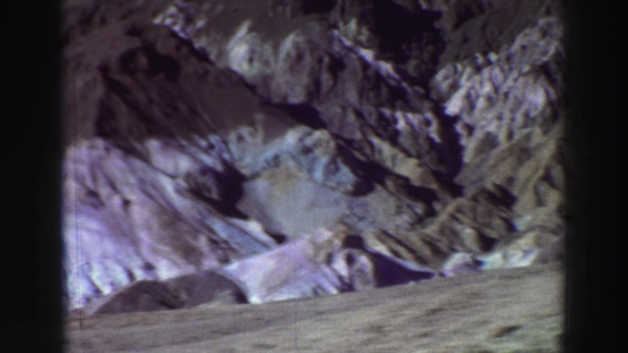 Rocky slope and pale ground seen through a dark 8mm film border.