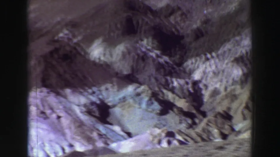 1969 Lake Tahoe 8mm frame showing rugged slope textures, pale earth, and a soft purple-gray archival film cast.