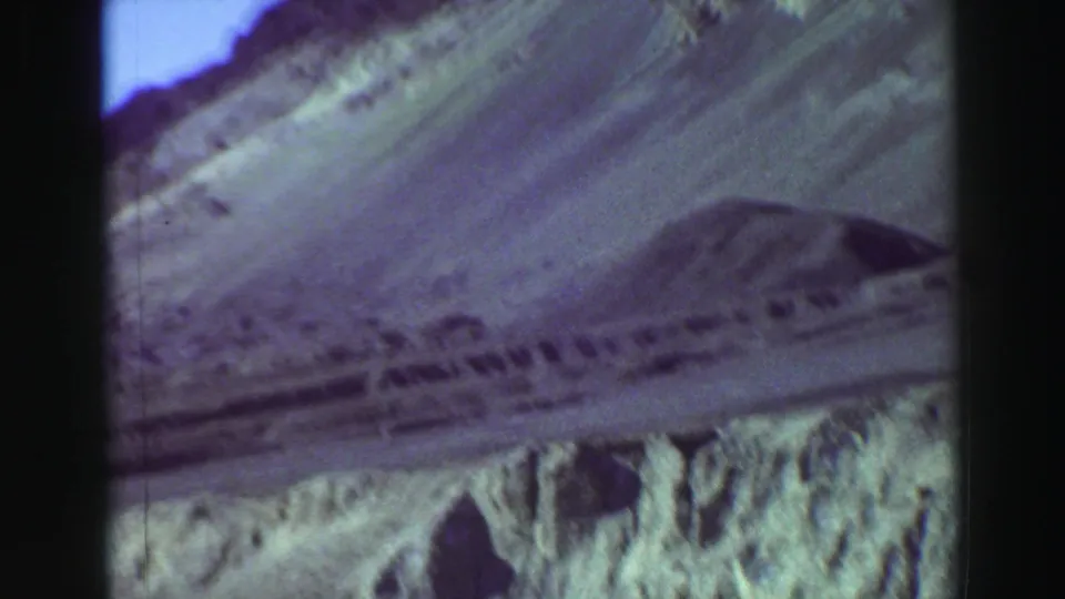 Soft, grainy 8mm frame showing a rocky hillside and pale track during a handheld scenic pan in the cataloged 1969 Lake Tahoe footage.