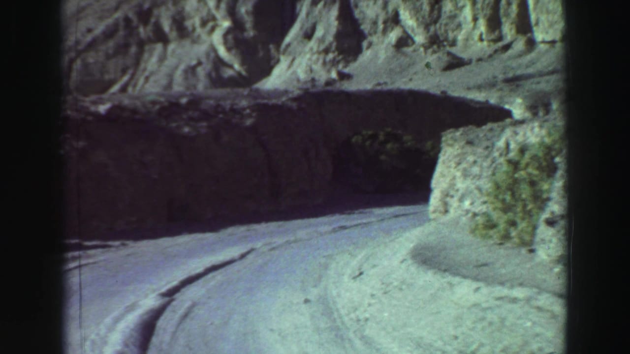 Forward view of a paved road curving through steep rocky terrain.