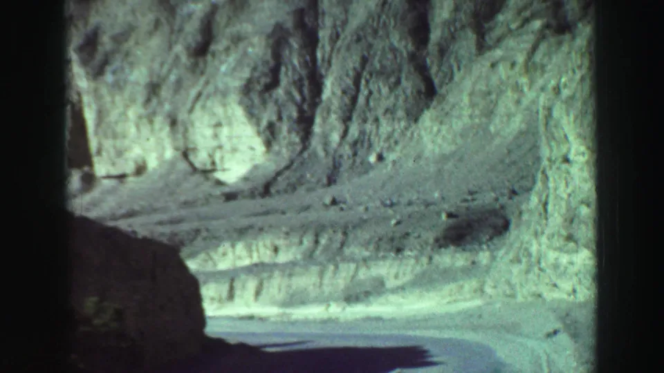 1969 8mm view near Lake Tahoe of a road continuing past pale, rugged rock walls and a dark foreground shadow.
