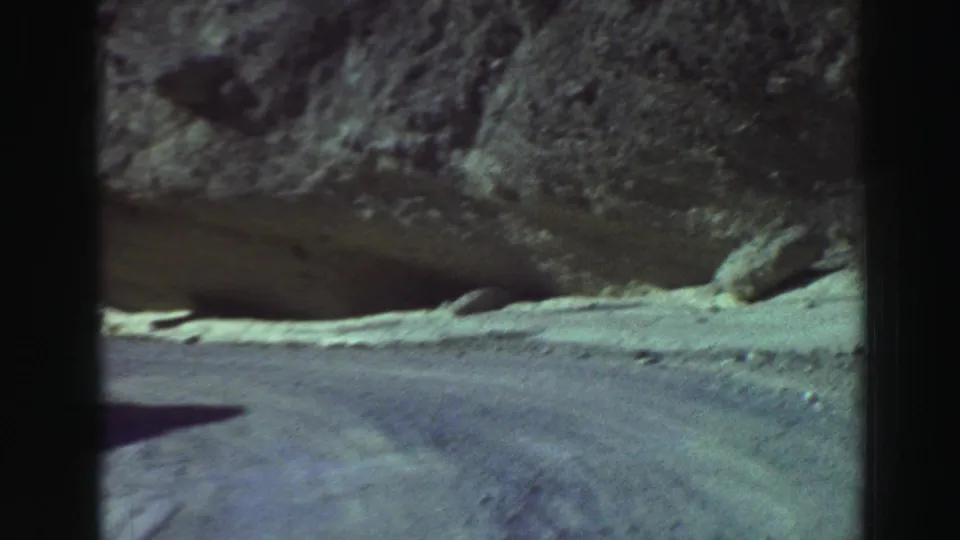 Car-window view from 1969 Lake Tahoe footage looking ahead on a pale dirt road through rugged mountain terrain.