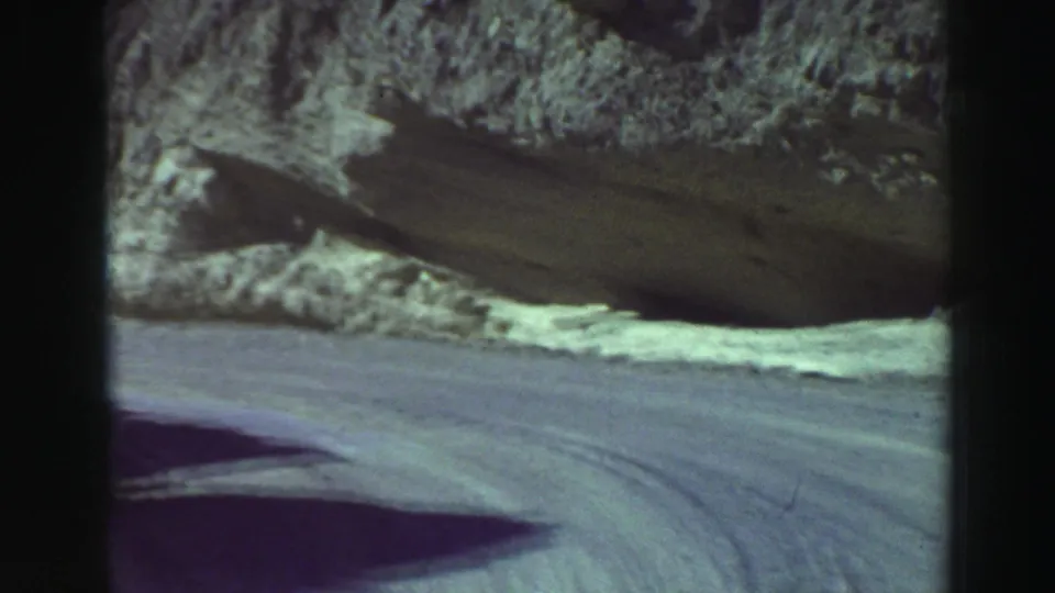 Vintage 8mm frame near Lake Tahoe showing a rocky roadside bank and the edge of a rough dirt road from a moving car.