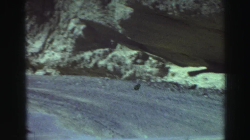 1969 8mm Lake Tahoe travel frame with a dusty mountain road passing a jagged rock face under daylight.