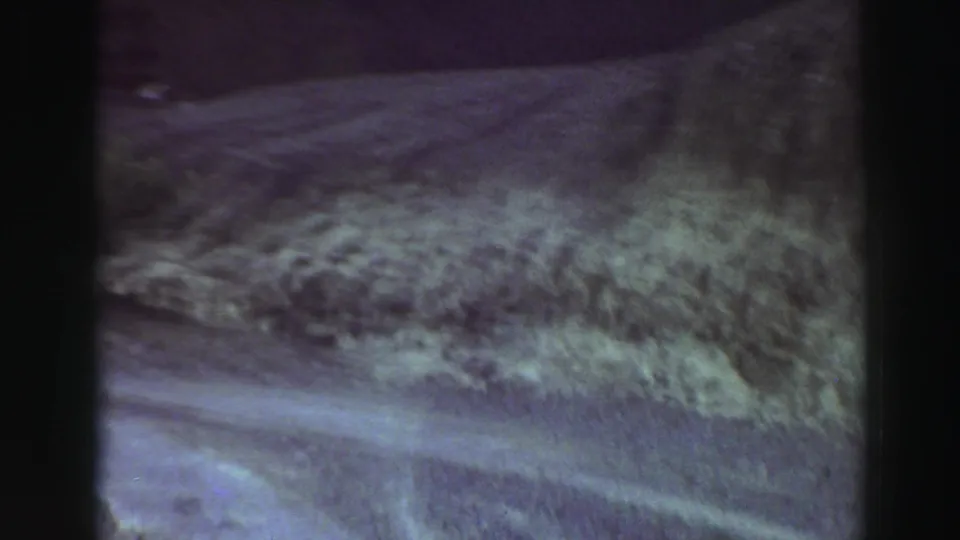 Soft, grainy 8mm view of roadside vegetation and mountain slope near Lake Tahoe, California, from a moving car.