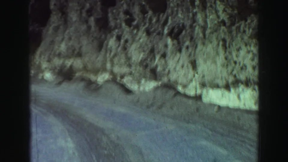 Vintage 8mm frame of a curving mountain road beside a rocky, brushy roadside near Lake Tahoe in 1969.