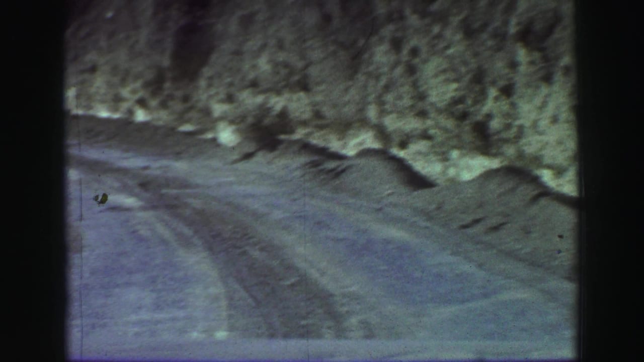 Muddy mountain road curving beside a rocky roadside cut.
