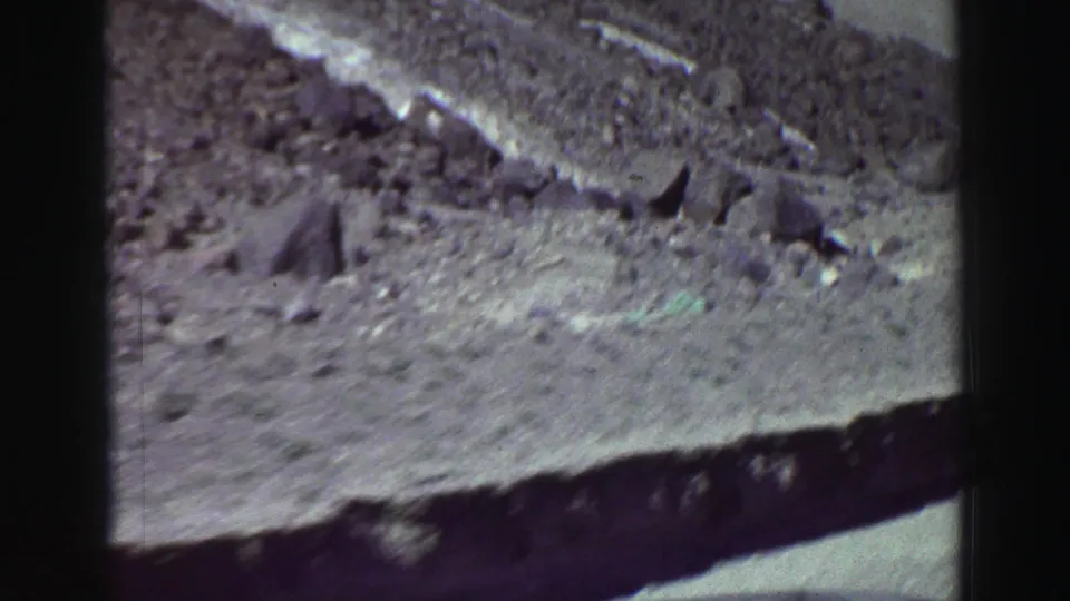 8mm frame from the Lake Tahoe-area road showing loose rocks, a rough shoulder, and a steep roadside slope.